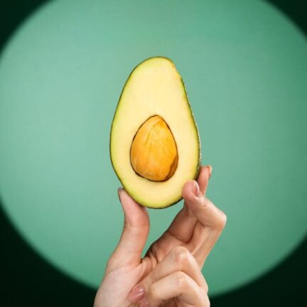 A fresh avocado half held by human hand against a green spotlight background.