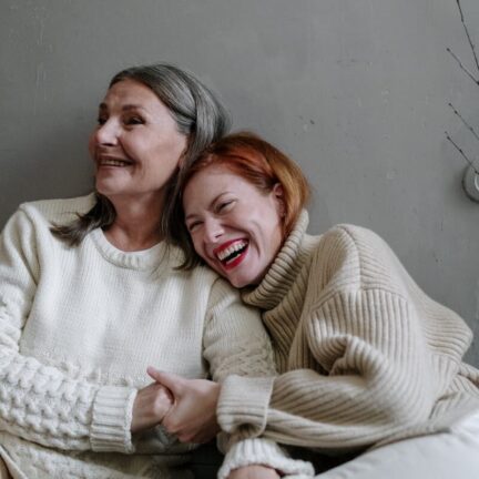 Mother and daughter in cozy sweaters sharing a moment of laughter, showcasing familial love.